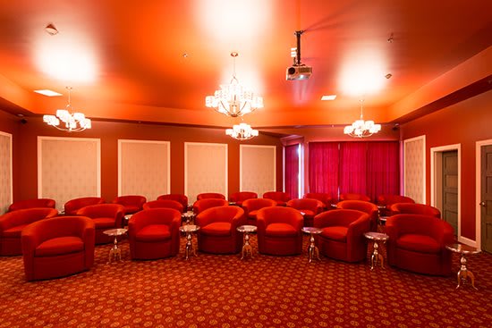 A cozy theater room with red chairs and elegant chandeliers.