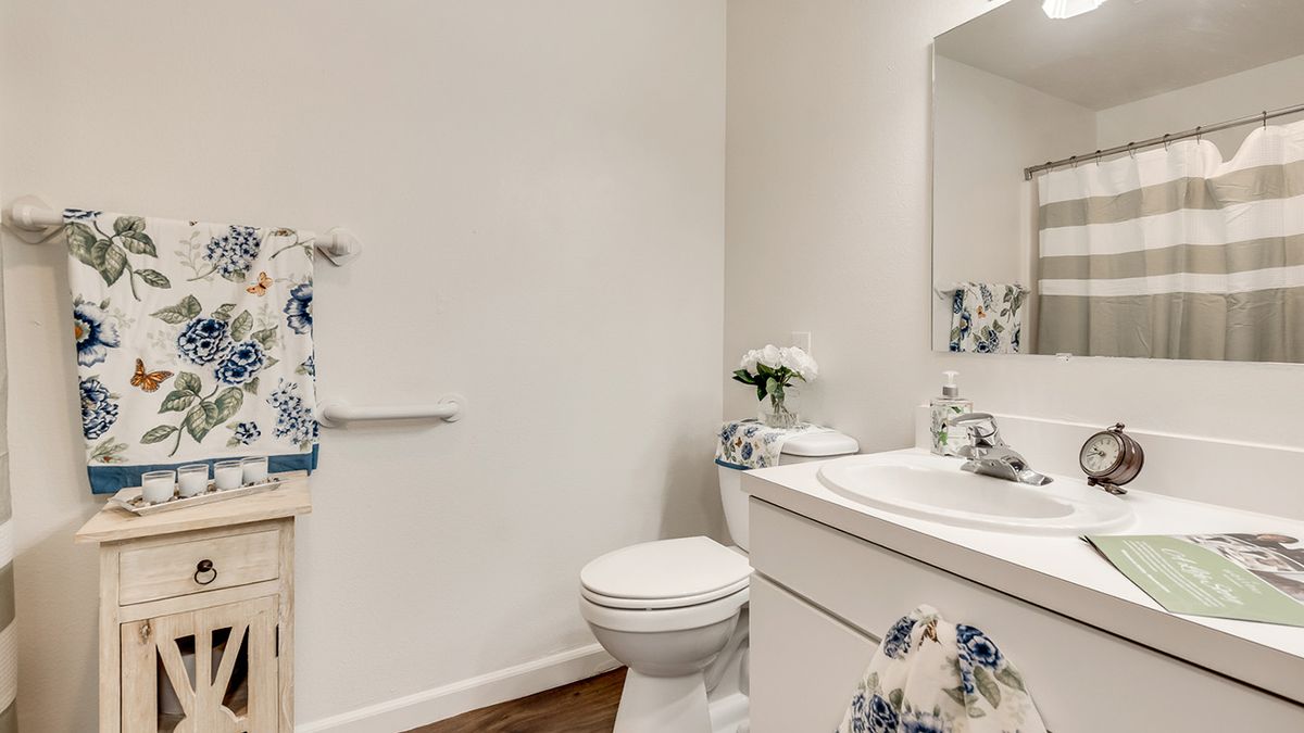 A neatly organized bathroom with a toilet, sink, and mirror, featuring floral decor.