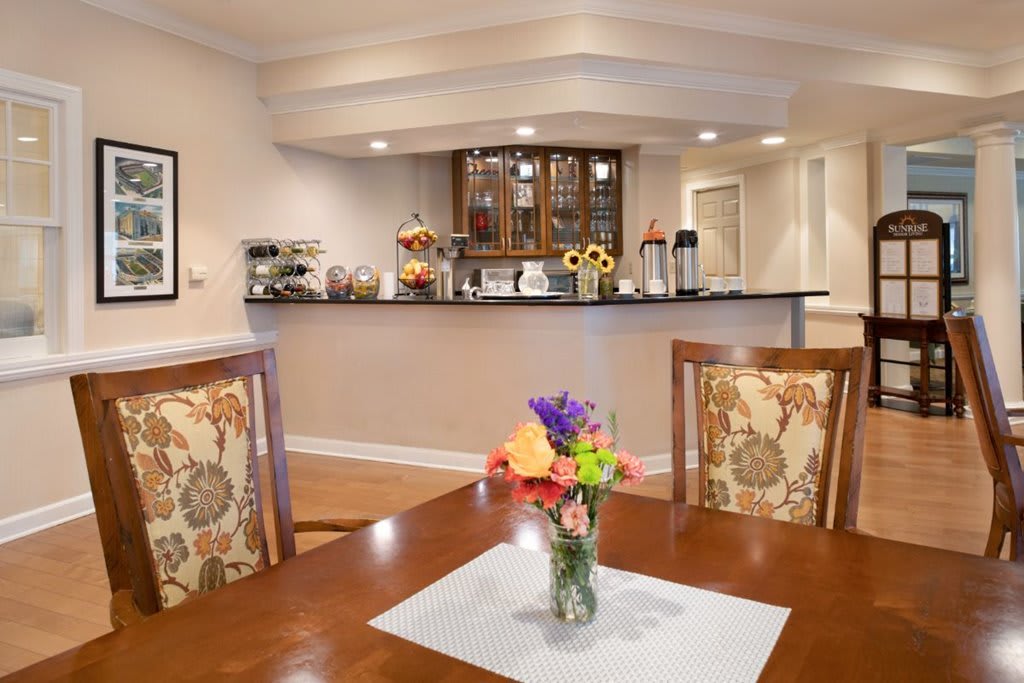A cozy dining area with a floral arrangement on the table and a modern bar counter in the background.