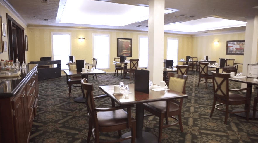 A spacious dining area with neatly arranged tables and chairs, carpeted flooring, and warm indoor lighting.