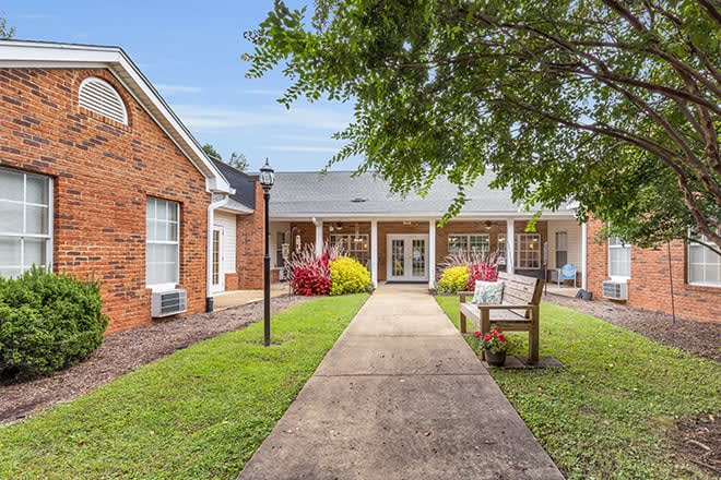 A charming brick building with a central walkway, flanked by well-maintained gardens and a cozy bench.