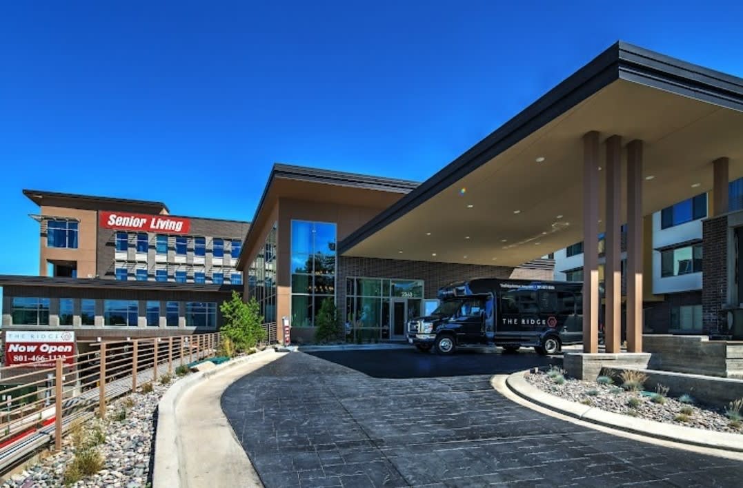 A modern hotel entrance with a van parked in the driveway under a clear blue sky.