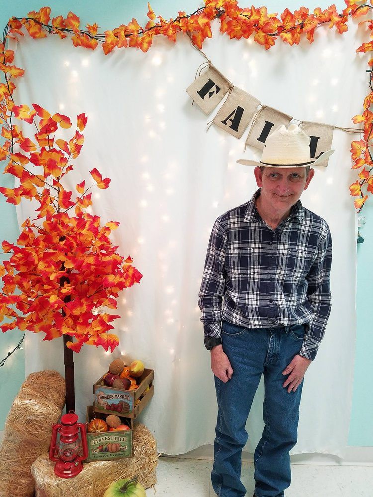 Person in a cowboy hat and plaid shirt enjoying fall decorations.