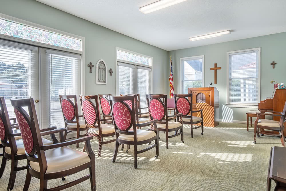 A small chapel with rows of chairs facing a podium and a cross on the wall.