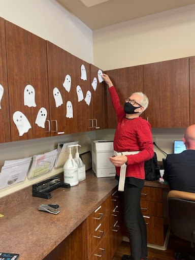 A fun Halloween decoration activity in the office, featuring paper ghosts and a person dressed in costume.