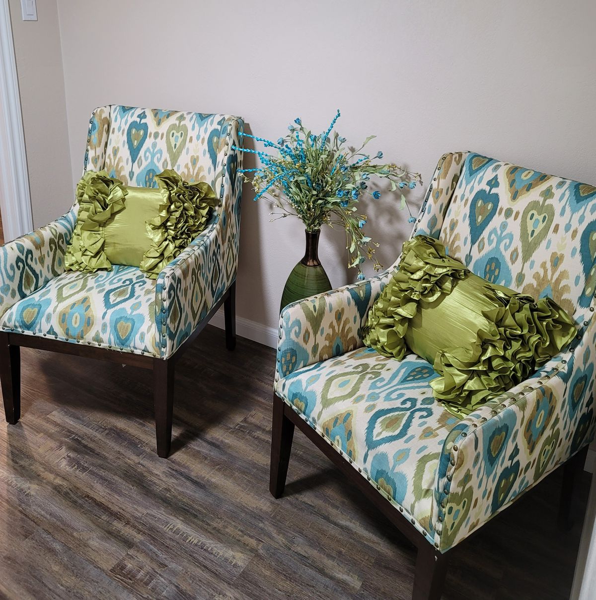 A cozy seating area featuring two patterned armchairs with green accent pillows and a decorative vase.