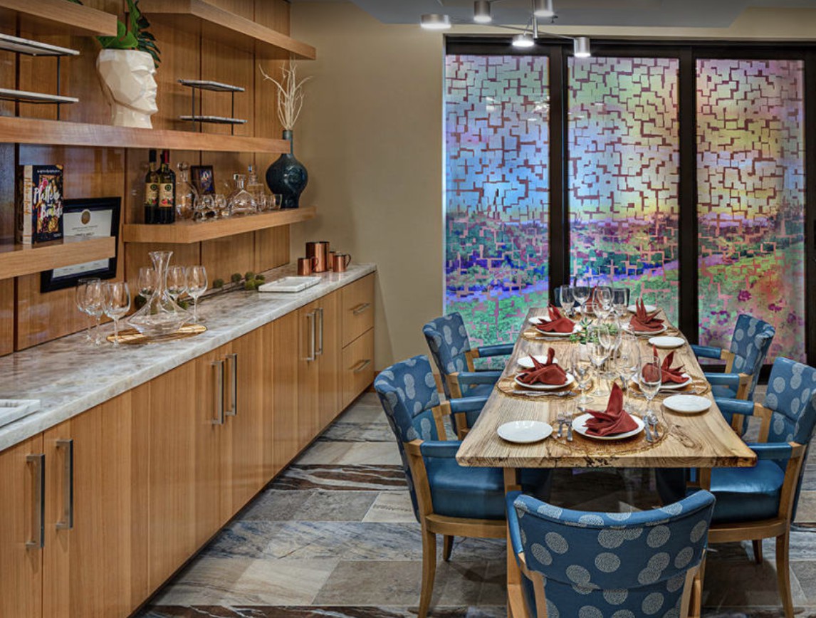 A modern dining room with a beautifully set table, featuring wooden shelves and colorful glass panels.