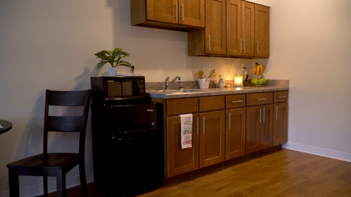 A cozy kitchen with wooden cabinets, a sink, microwave, and a small refrigerator.
