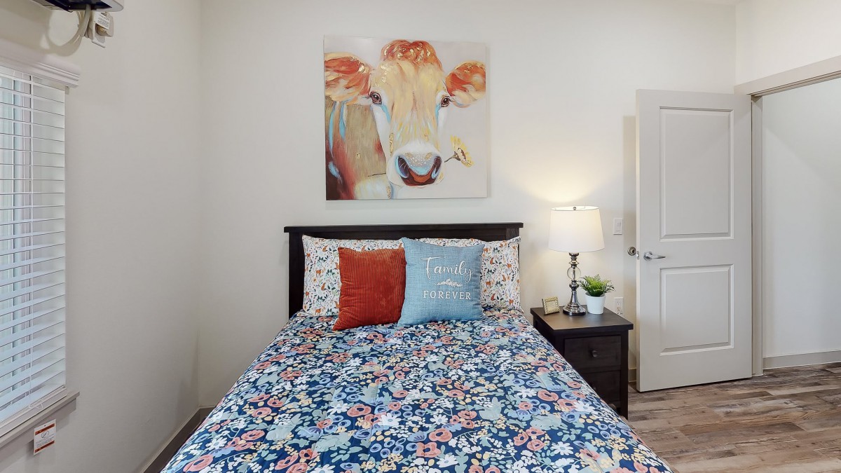 A cozy bedroom featuring a colorful cow painting above the bed with floral bedding and decorative pillows.