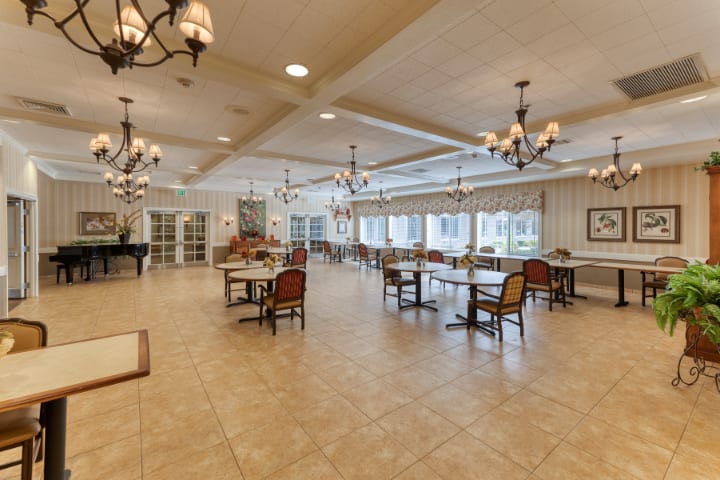 A spacious dining hall with elegant chandeliers, neatly arranged tables and chairs, and a warm, inviting atmosphere.