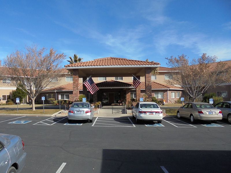 A view of a building entrance with American flags and parked cars in front.