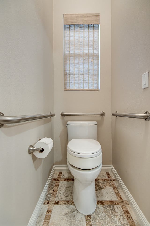 A small bathroom with a toilet, equipped with grab bars and a toilet paper holder.