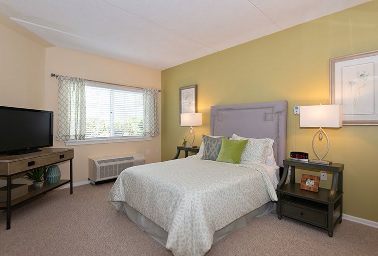 A cozy bedroom with a neatly made bed, nightstands, lamps, and a window with curtains.