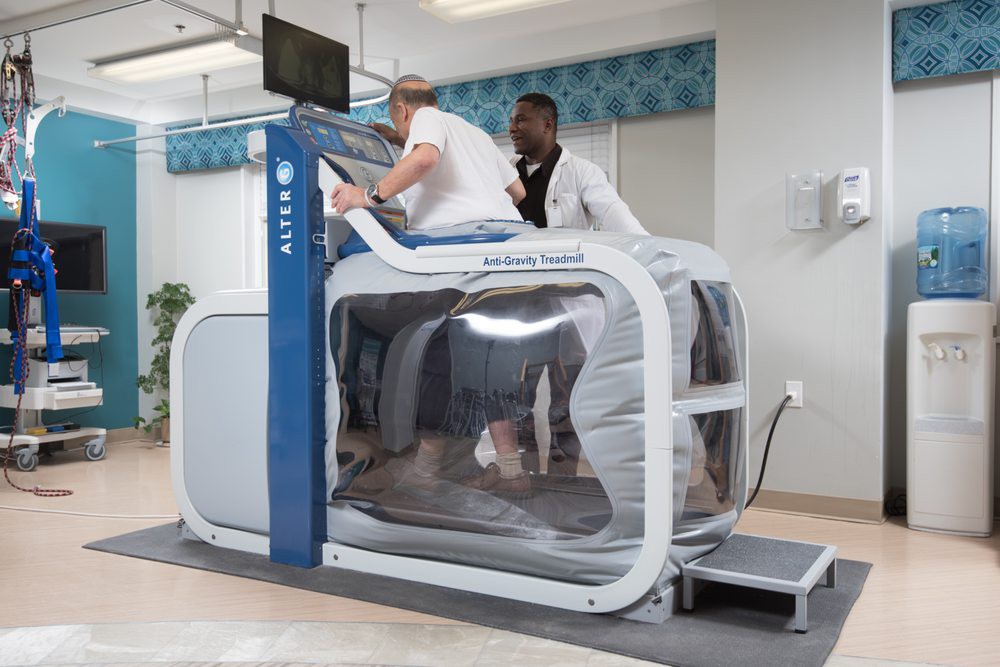 A person using an anti-gravity treadmill under the supervision of a trainer in a rehabilitation setting.