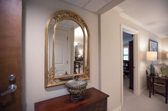 A hallway with a decorative mirror above a wooden table, featuring an ornate vase.