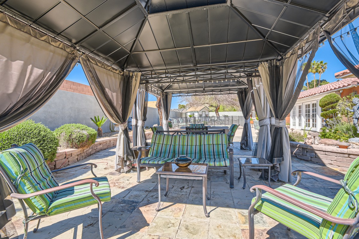 A cozy outdoor patio area with a gazebo providing shade over comfortable seating and a table.
