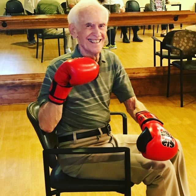A senior man sitting in a chair wearing boxing gloves, ready for exercise.