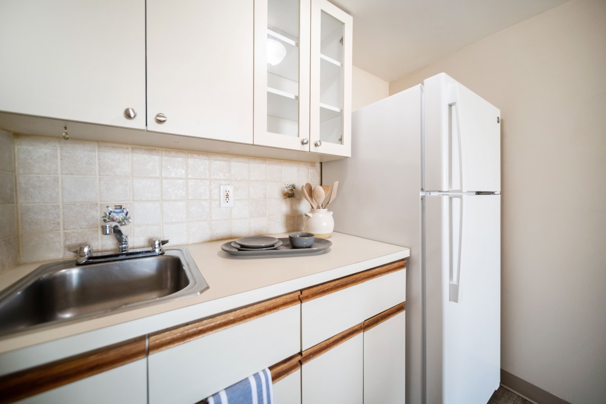 A minimalist kitchen with white cabinets and a refrigerator, featuring a clean countertop and sink.