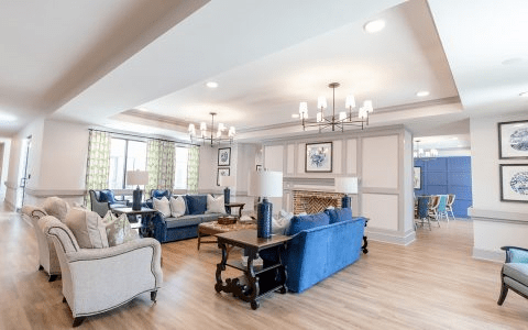 A spacious and elegantly decorated living room with blue sofas, chandeliers, and wood flooring.