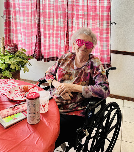 An elderly woman enjoying a festive moment at the dining table, complete with pink sunglasses and vibrant decorations.