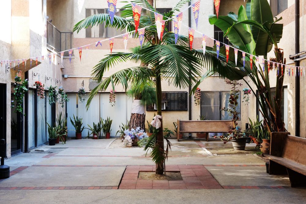 A quaint courtyard decorated with flags and a central palm tree, surrounded by benches and potted plants.