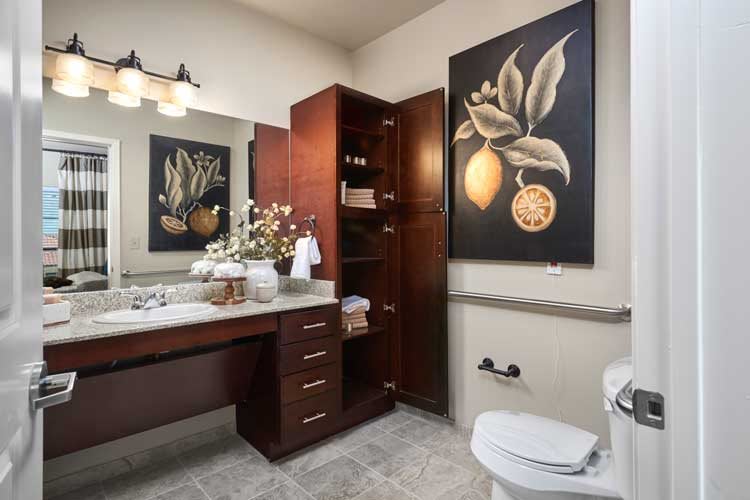 A well-designed bathroom with wooden cabinets, wall art, and decorative flowers.
