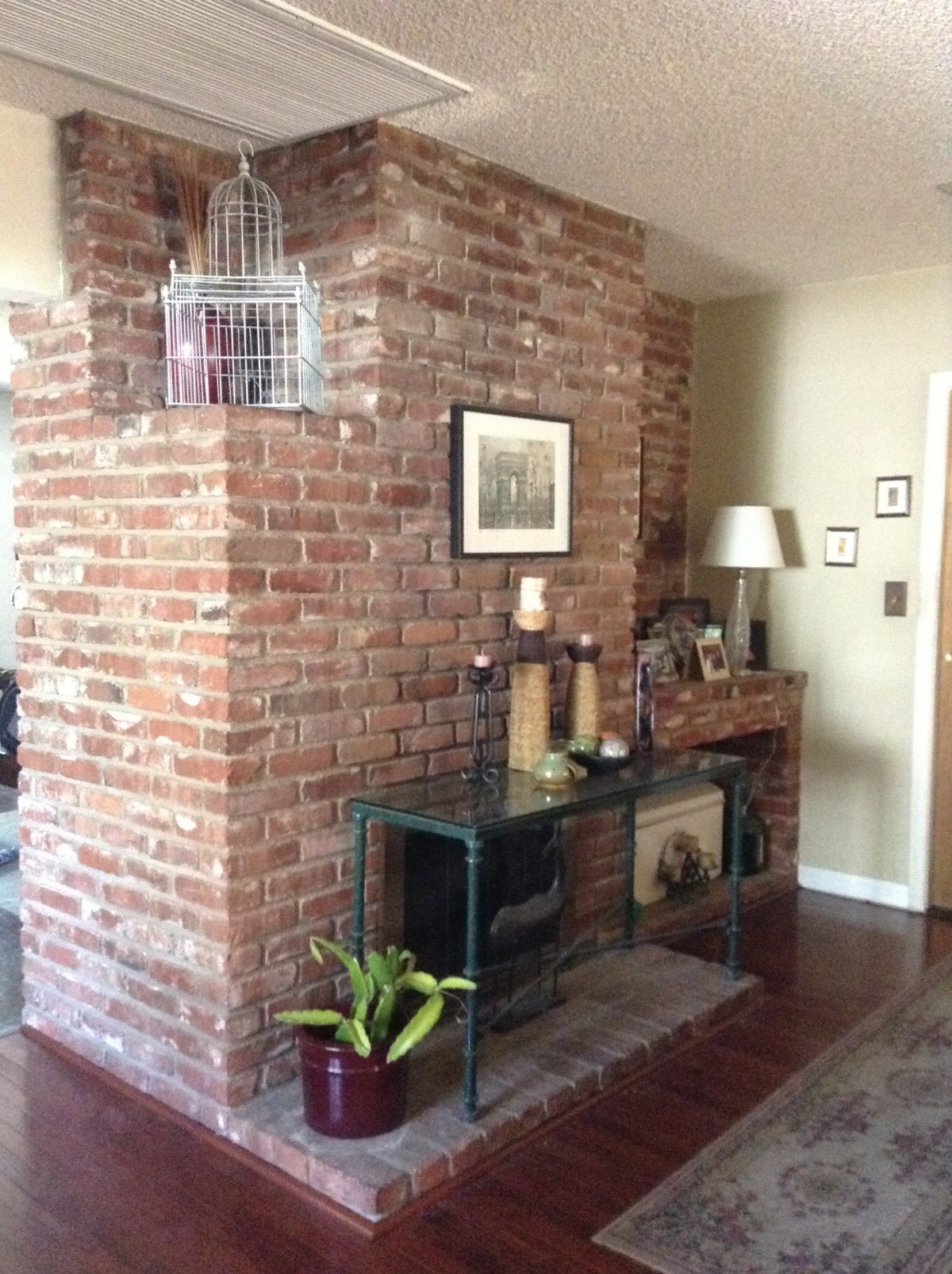 A cozy interior with an exposed brick wall, featuring a console table, decorative items, and a hanging birdcage.