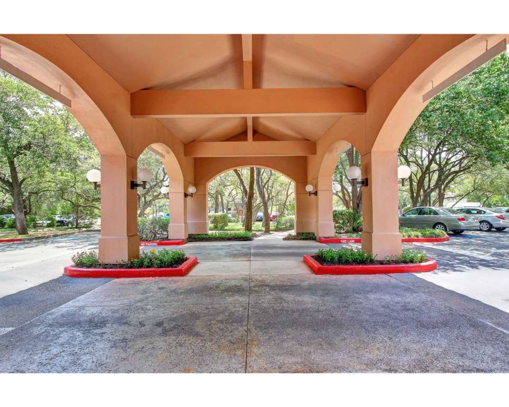 A covered driveway with multiple archways and neatly landscaped surroundings.