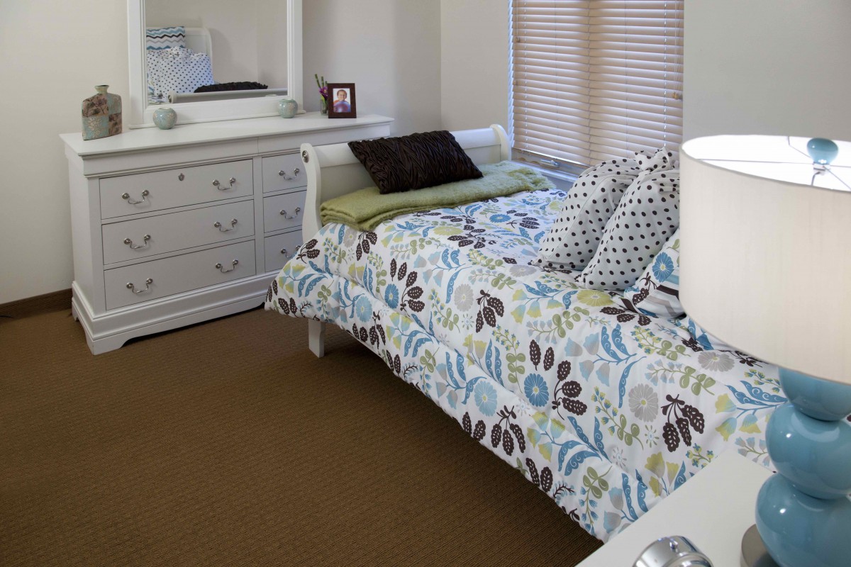 A cozy bedroom with a floral-patterned bedspread and a matching dresser with a mirror.
