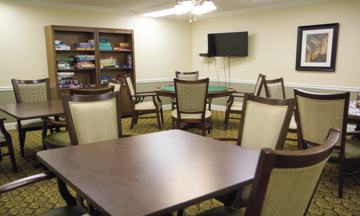 A meeting room with tables, chairs, a television, and a bookshelf.