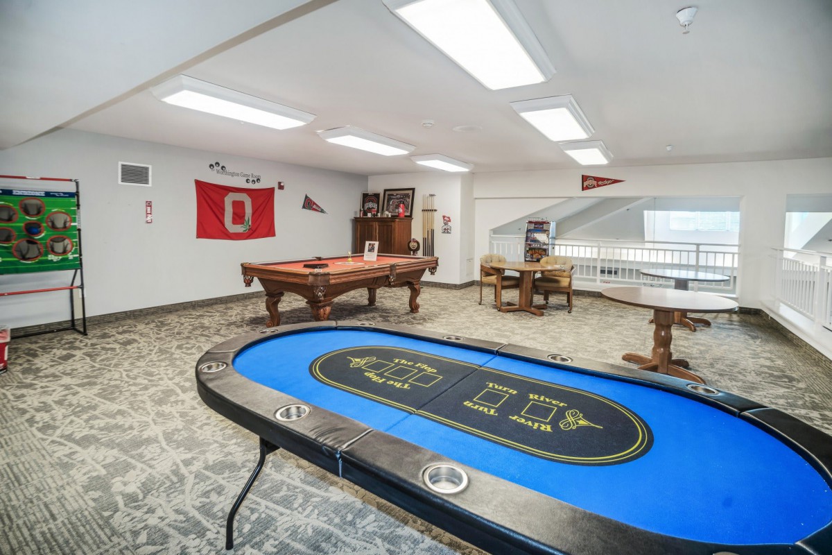 A spacious game room featuring a poker table and a pool table, adorned with various flags on the walls.