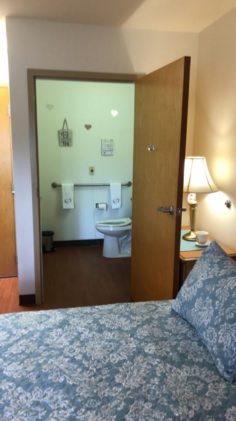 A cozy bedroom with an open door leading to a bathroom, featuring a lamp and neatly arranged towels.