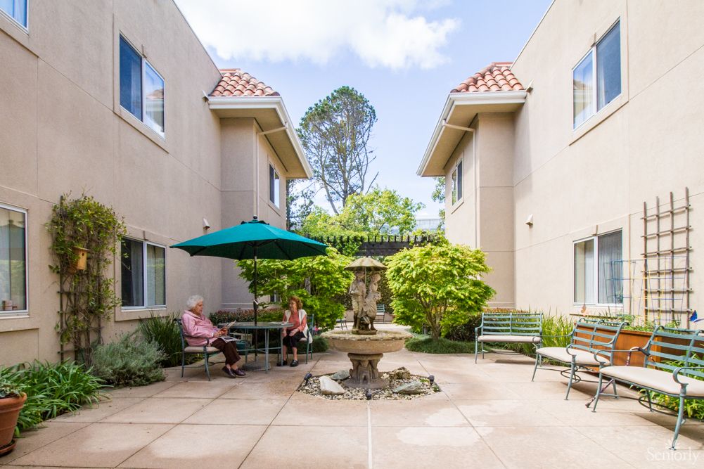 A serene courtyard with a fountain and outdoor seating, surrounded by two buildings.