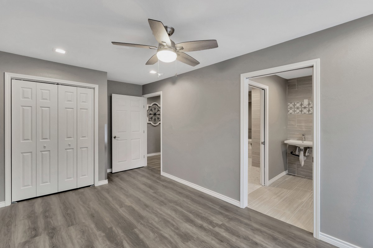 A modern bedroom featuring laminate flooring, a ceiling fan, and neutral color palette. The room includes a closet and an en-suite bathroom.