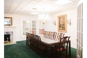 A well-lit dining room with a large table, surrounded by chairs and adorned with a chandelier and artwork.