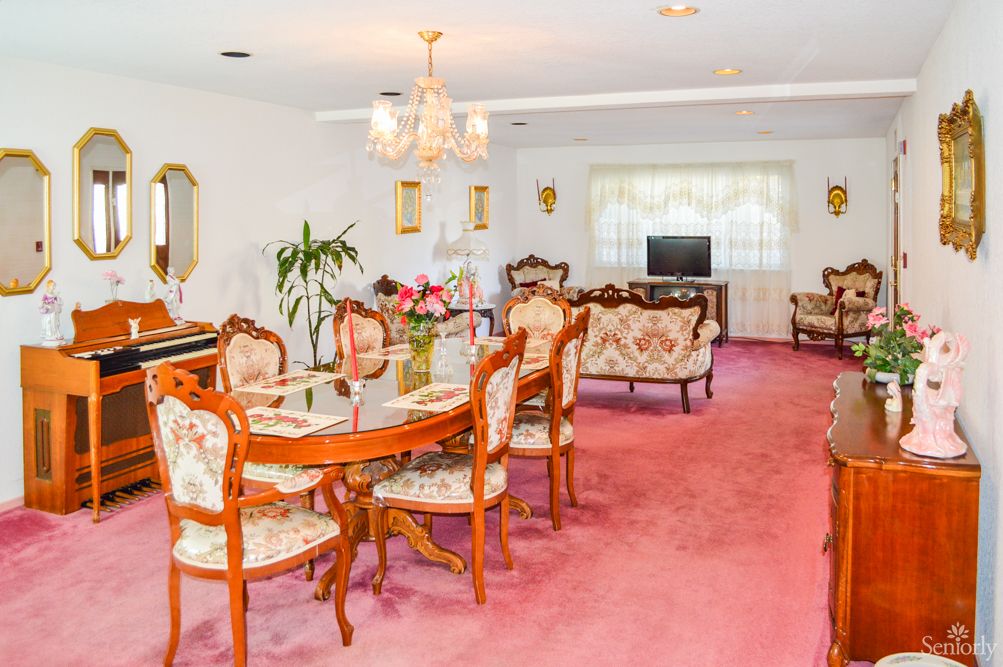 A vintage-style dining room with floral upholstered furniture and a pink carpet.
