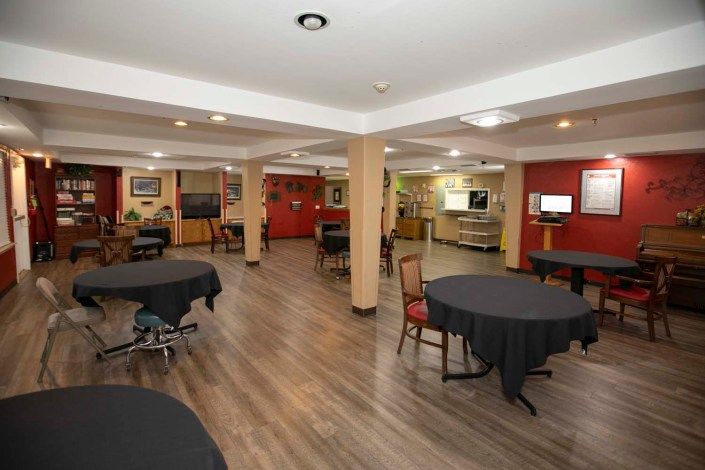 A spacious indoor dining area with wooden flooring, featuring tables and chairs arranged neatly under soft lighting.
