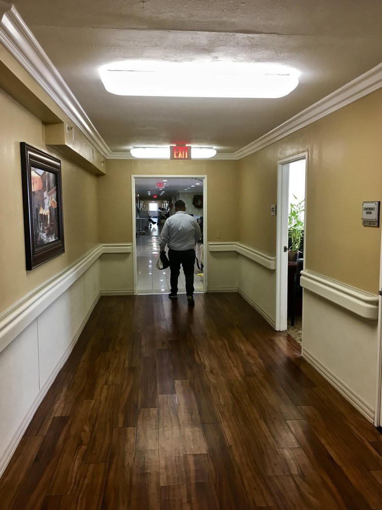 A person walks down a well-lit hallway with wooden floors and framed artwork on the walls.