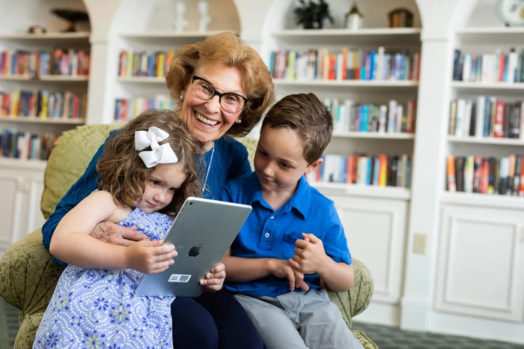 A joyful grandmother with her two grandchildren enjoying a tablet together in a cozy room.