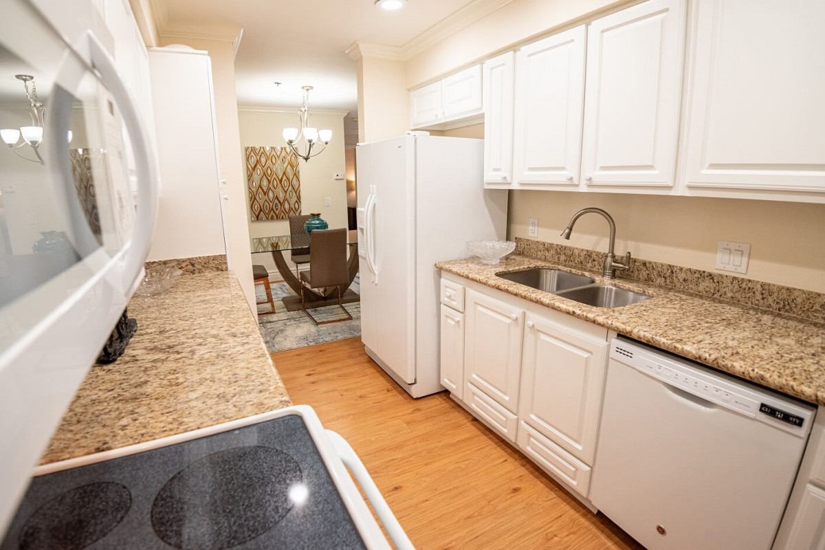 A modern kitchen with white cabinets, granite countertops, and a view into the dining area.
