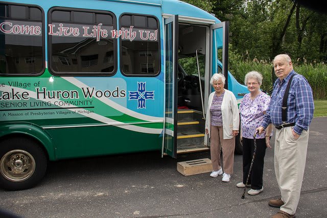 A group of elderly women standing next to a community transport bus.