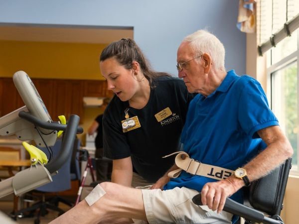 A healthcare professional assists an elderly person during a physical therapy session.