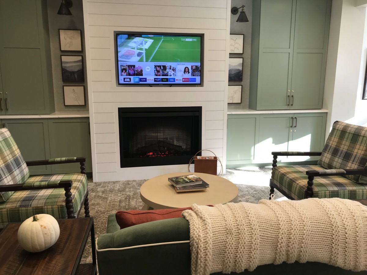 A cozy living room with a TV mounted above a fireplace, surrounded by comfortable seating and a central coffee table.