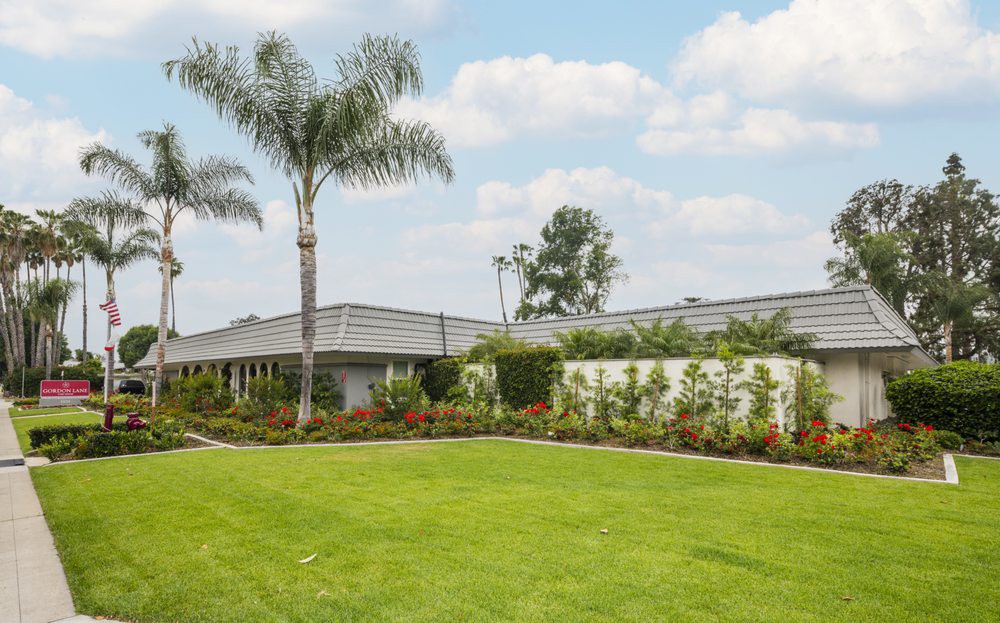 A suburban house with a large, well-maintained lawn and a palm tree under a cloudy sky.
