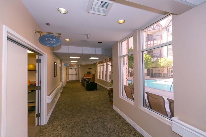 A well-lit hallway with large windows overlooking a swimming pool and seating area.