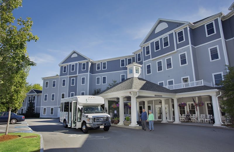 A large, multi-story building with a shuttle bus parked in front and people entering.