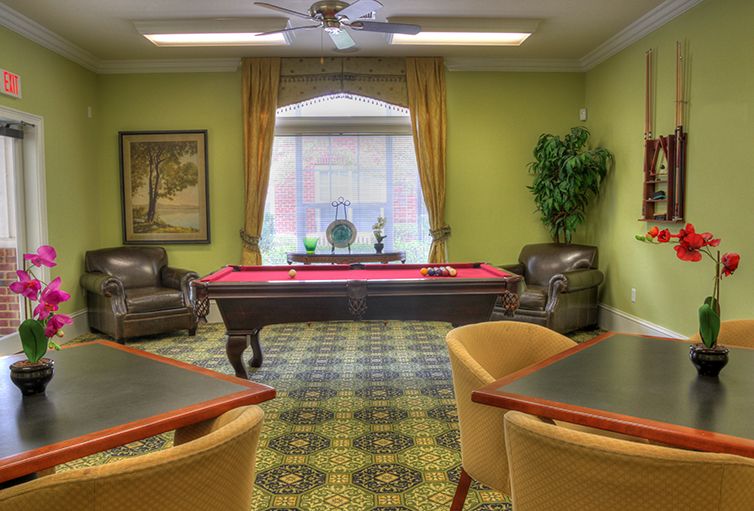 A cozy billiards room with a red pool table, surrounded by comfortable chairs and sofas, decorated with green walls and elegant curtains.