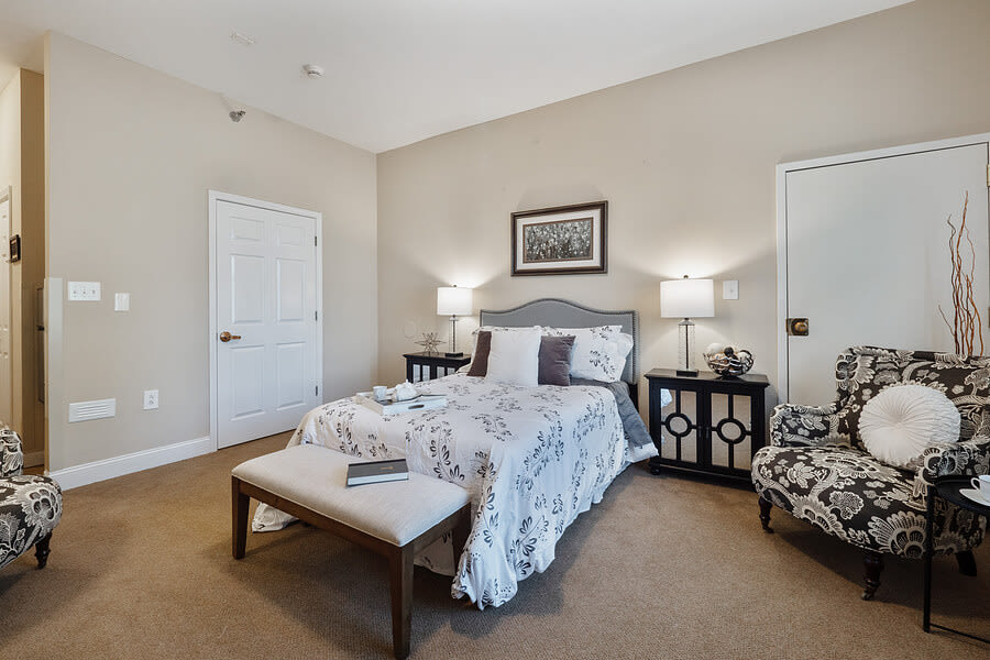 A cozy bedroom featuring a neatly made bed with decorative pillows, nightstands with lamps on both sides, and a comfortable chair in the corner.