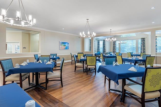 A spacious dining area with elegantly set tables and chairs, illuminated by chandeliers.