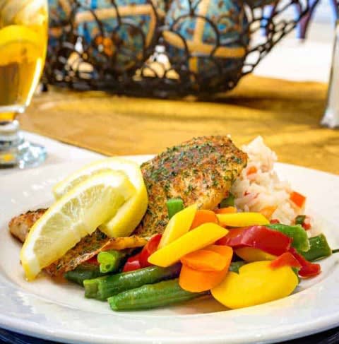 A plate of grilled fish topped with a lemon slice, served with colorful vegetables.